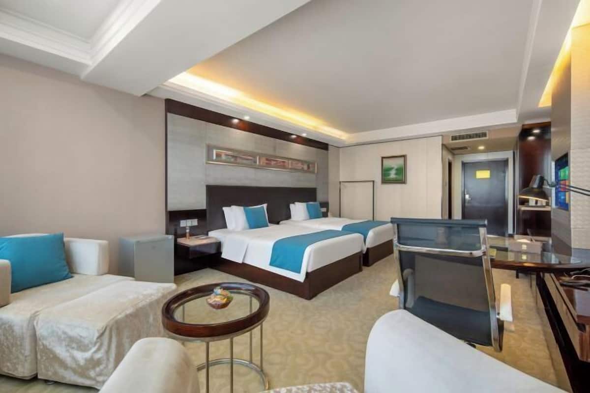 Ein Hotelzimmer mit zwei Betten, einem Schreibtisch, einem Stuhl, einer Couch und einem kleinen Tisch.