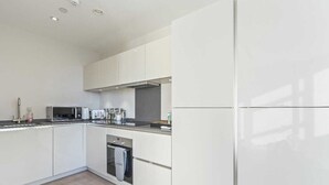 A modern kitchen with white cabinetry, a built-in oven, and a microwave. - Heathrow Retail Park Apartment Sleeps SEVEN Turbo Wi-Fi (Shepperton)