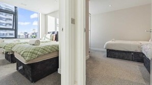 A modern bedroom with two beds, a large window, and a view of buildings. - Heathrow Retail Park Apartment Sleeps SEVEN Turbo Wi-Fi (Shepperton)