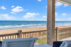 A beach view from a covered area with a wooden railing, a stop sign, and a glimpse of the ocean. - Beachfront Home | Direct Beach Access | Gulf Views | Large Deck | Pet Friendly (Gilchrist)