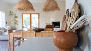Una cuina amb una illa central, llums pendents de fusta i una gerra de terrissa rústica amb utensilis.