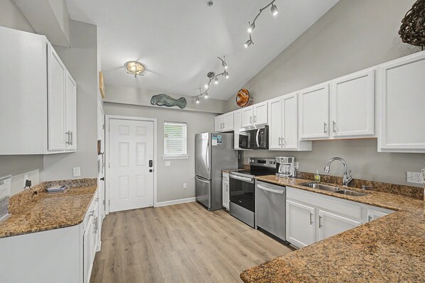 A kitchen with white cabinets, stainless steel appliances, granite countertops, and a wooden floor. - Coastal Condo with Bay Views- Baywatch H6 (Pensacola Beach)