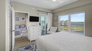 Un dormitorio con una cama grande, televisión, cómoda, una silla y vista al agua.