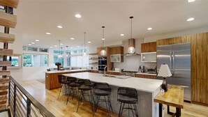 A modern kitchen with a large island, bar stools, stainless steel appliances, and wooden cabinetry.