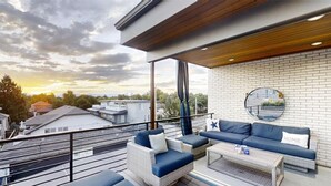 A balcony with a sofa, chairs, and a coffee table, overlooking a cityscape at sunset.