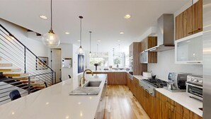 A modern kitchen with a central island, stainless steel appliances, wooden cabinets, and pendant lighting.