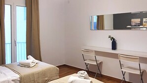 Habitació d'hotel amb dos llits, un escriptori, una cadira, un mirall i una finestra amb cortines.