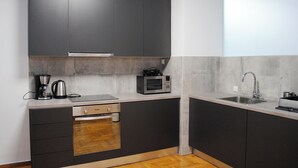 Una cuina moderna amb els elements inferiors fosc, un forn de mur, un microones, una cafetera i un rentaplat.