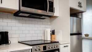 Una cocina moderna con gabinetes blancos, estufa de acero inoxidable, microondas y refrigerador.