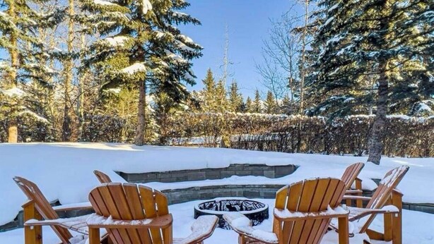 Un espacio al aire libre cubierto de nieve con sillas de madera y un pozo de fuego circular.