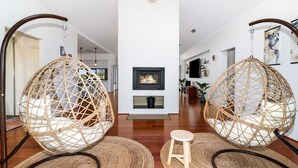 Un intérieur moderne agrémenté de deux grands fauteuils suspendus en fibres tressées, d’une cheminée et d’un style de décoration minimaliste.