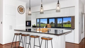 Une cuisine moderne dotée d’un grand îlot central, de tabourets de bar, de luminaires suspendus et offrant une vue sur un paysage verdoyant.