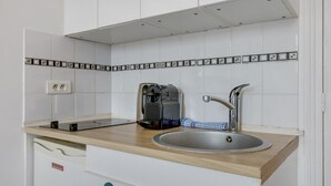 A kitchen with white cabinets, a stainless steel sink, a coffee maker, and a dish drying rack.