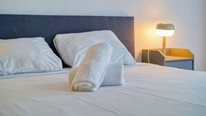 Un lit bien fait, avec du linge de lit blanc et des serviettes pliées, une lampe de chevet et une tête de lit moderne.