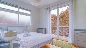 Une chambre moderne avec un grand lit, des tables de chevet, une petite table et une vue sur l’extérieur grâce à une porte-fenêtre coulissante.