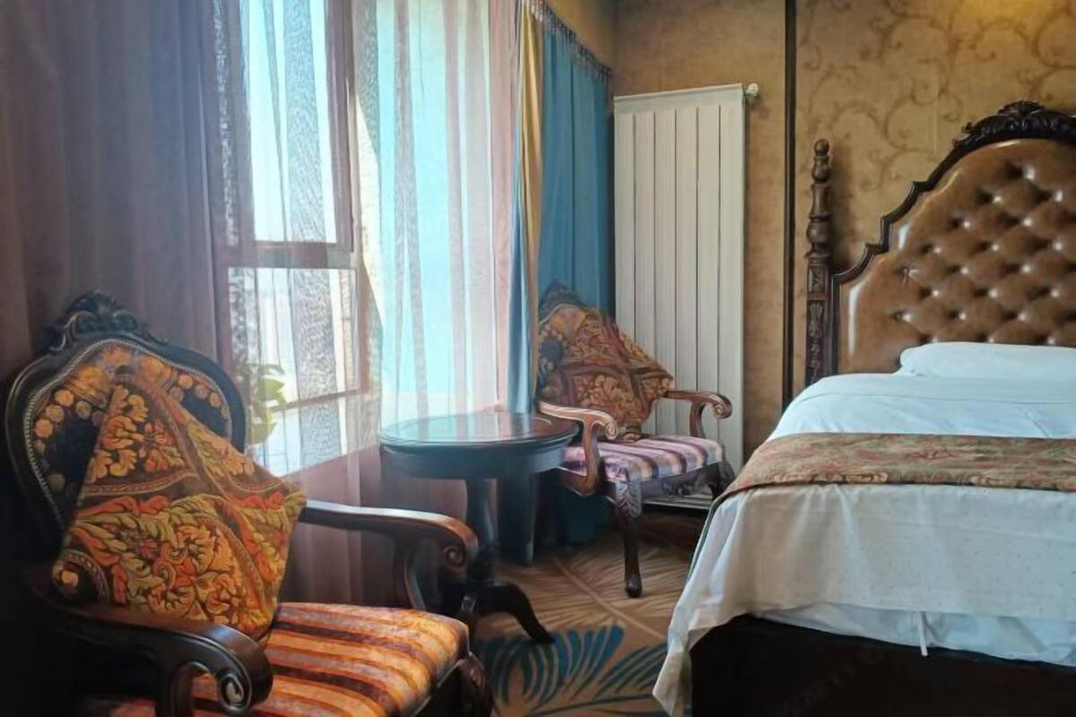 A room with a bed, two chairs, a small table, and a window with curtains.