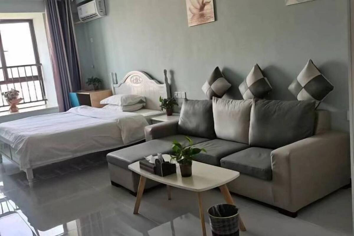 A modern room with a bed, a sofa, a small table, and a potted plant.