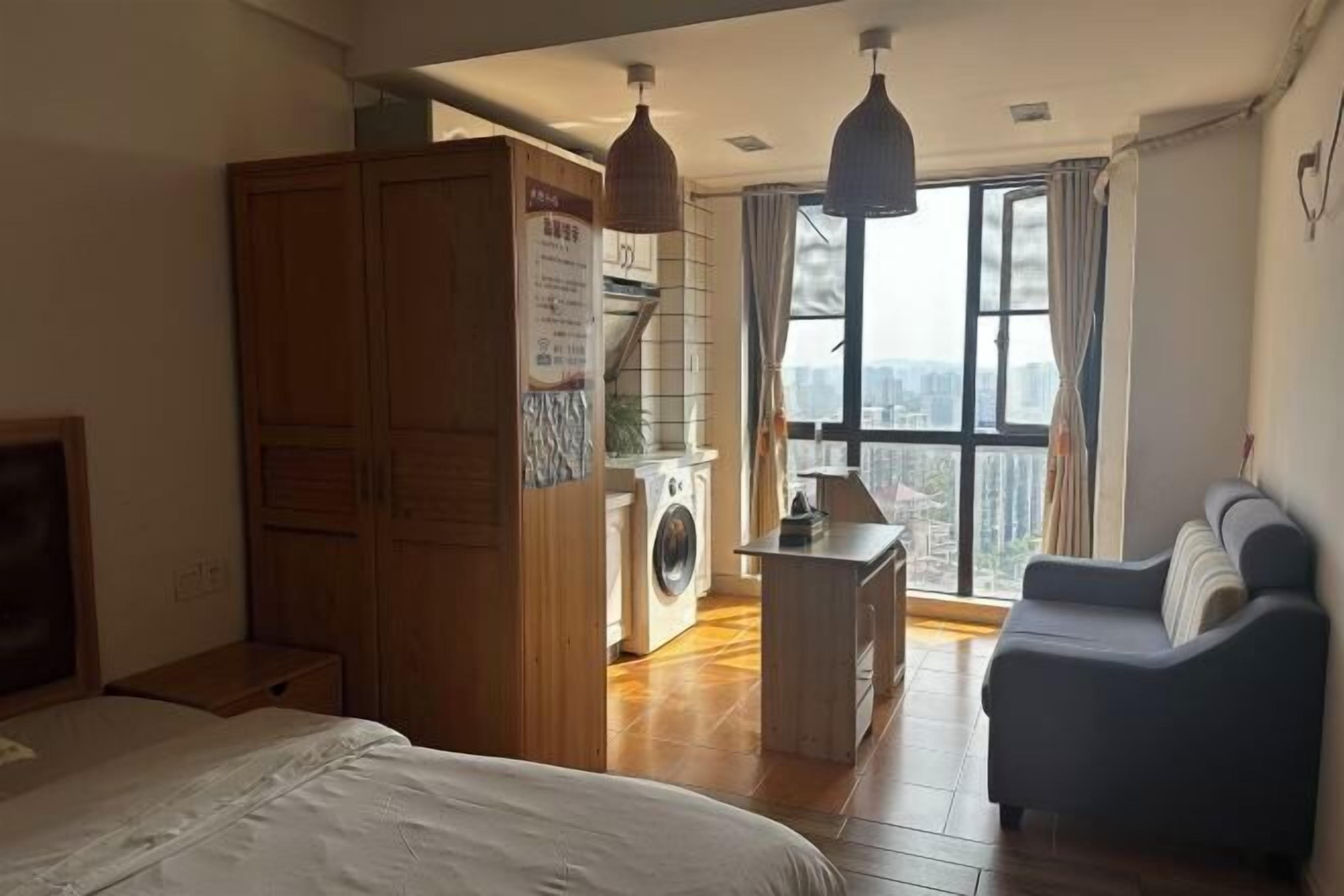 A bedroom with a bed, a wardrobe, a washing machine, a small table, and a sofa.
