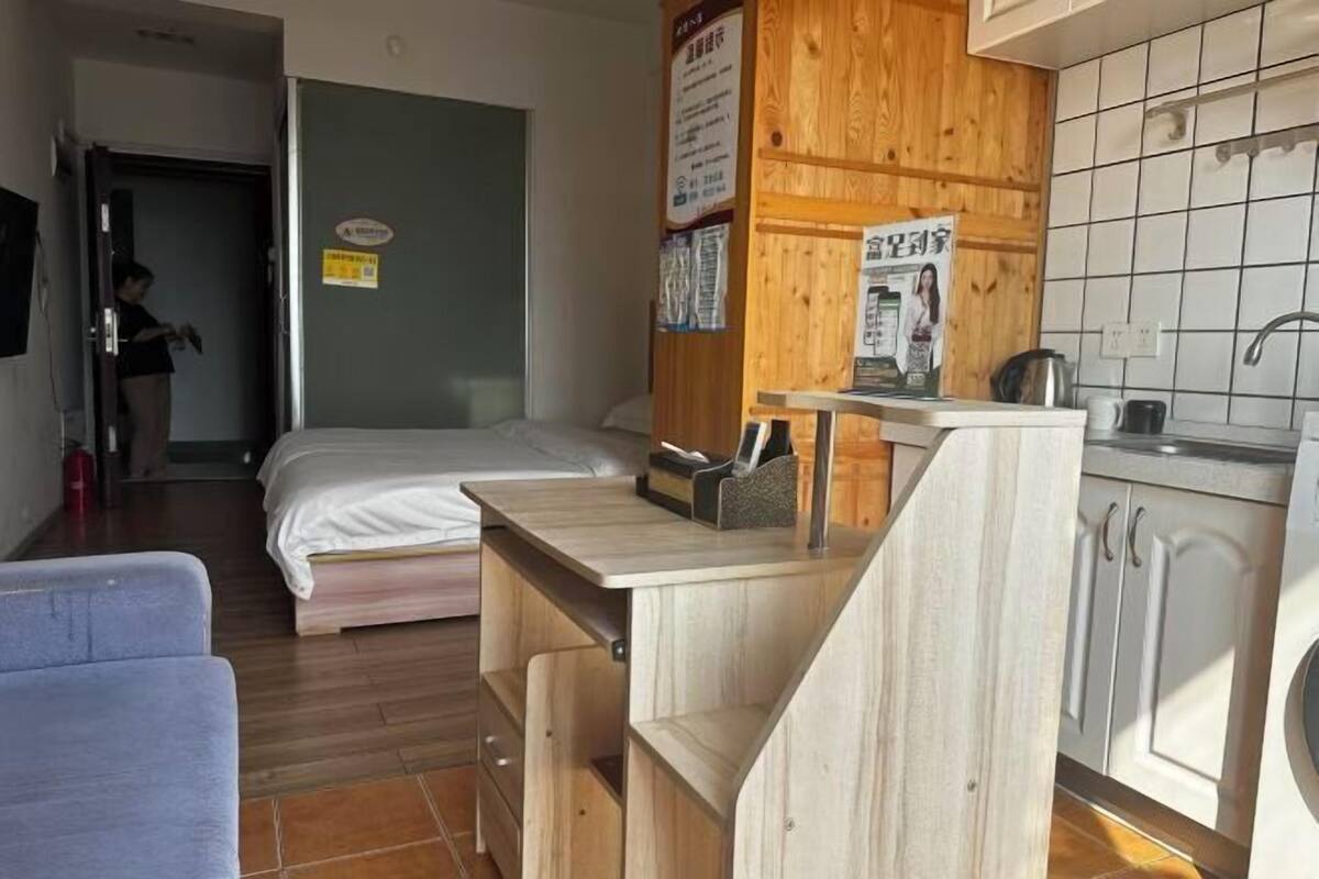 A compact room with a bed, a small kitchenette, and a chair.