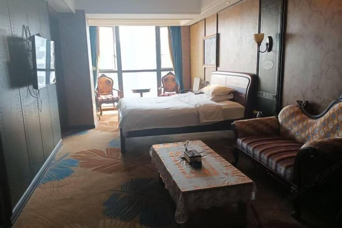 A hotel room with a bed, a sofa, a coffee table, and a view of the outside.