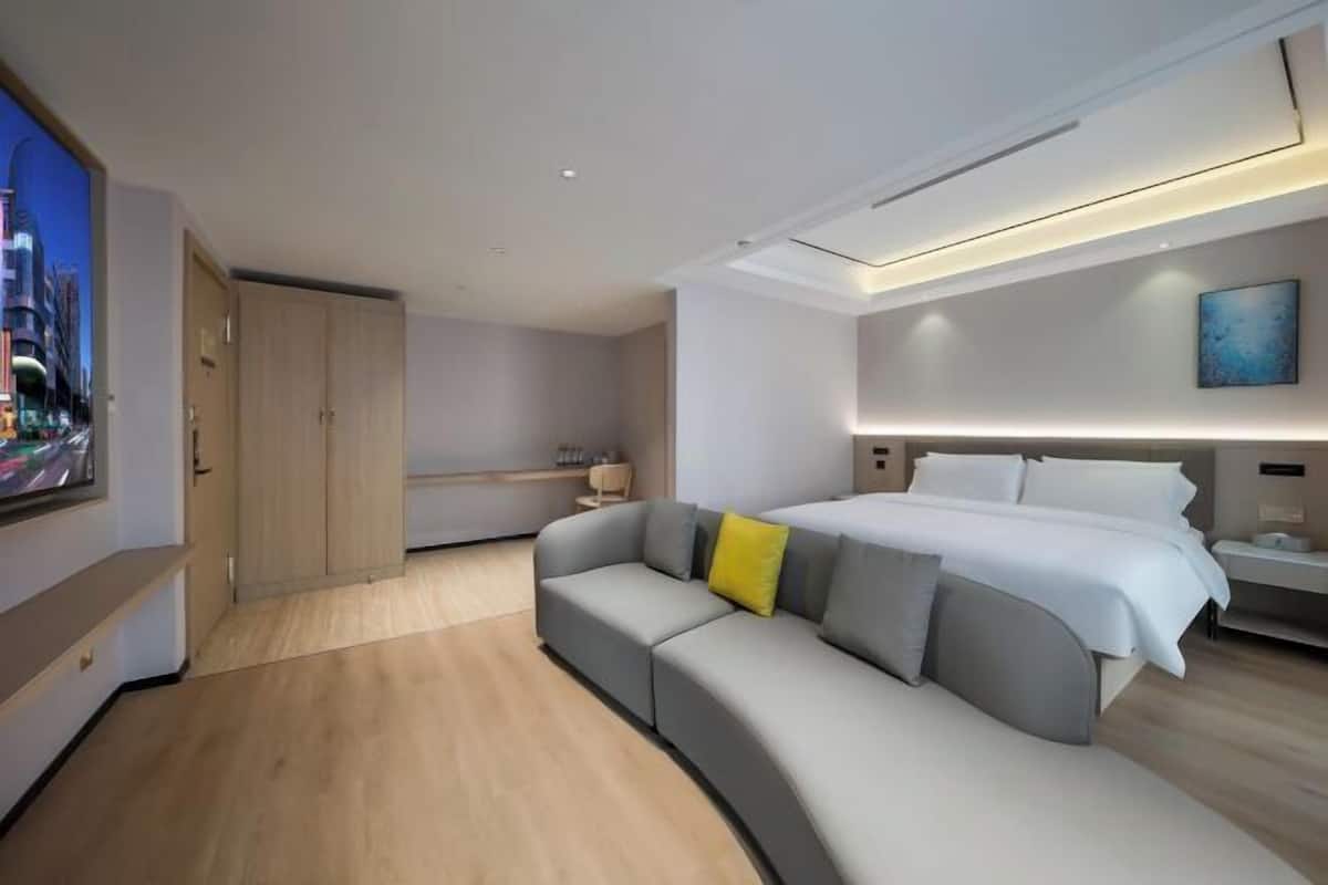 Ein modernes Hotelzimmer mit einer gebogenen grauen Couch, einem großen Bett, einem Nachttisch und einem Bild an der Wand.