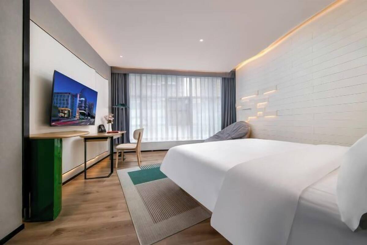 Ein Hotelzimmer mit Bett, Schreibtisch, Stuhl, Fernseher und einem Fenster mit Vorhängen.