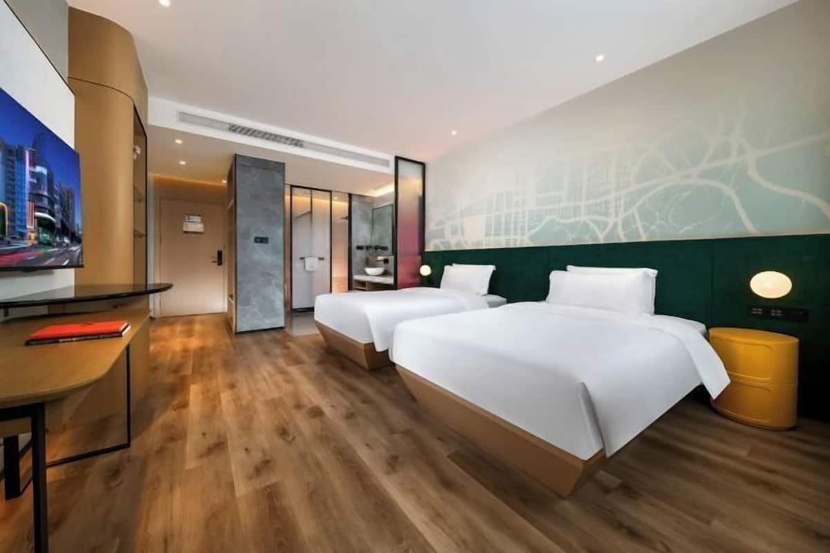 Ein Hotelzimmer mit Holzboden, zwei Betten, einem Schreibtisch, einem Fernseher und einer Wand mit einer Weltkarte.