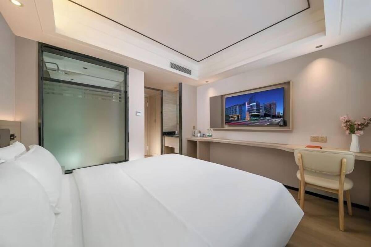 Ein Hotelzimmer mit Bett, Schreibtisch, Stuhl, einem Gemälde und einem Fenster.