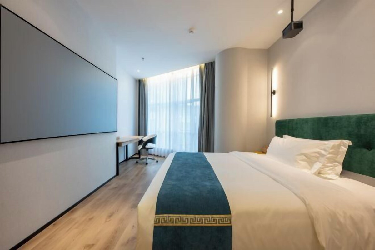 A modern hotel room with a large bed, a desk, and a projector screen on the wall.