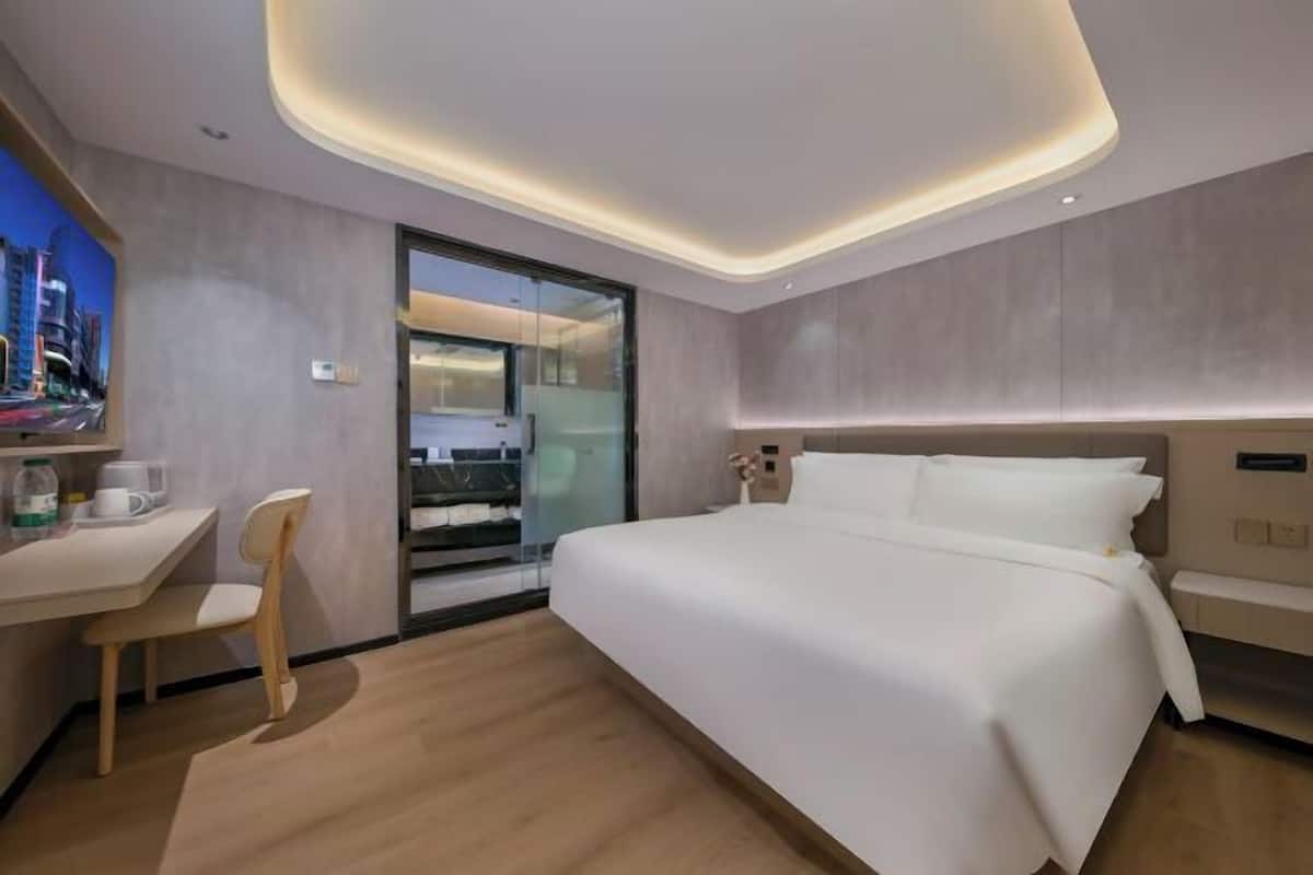 Ein modernes Hotelzimmer mit einem großen Bett, einem Schreibtisch mit Stuhl und einer Glastür, die auf einen Balkon führt.