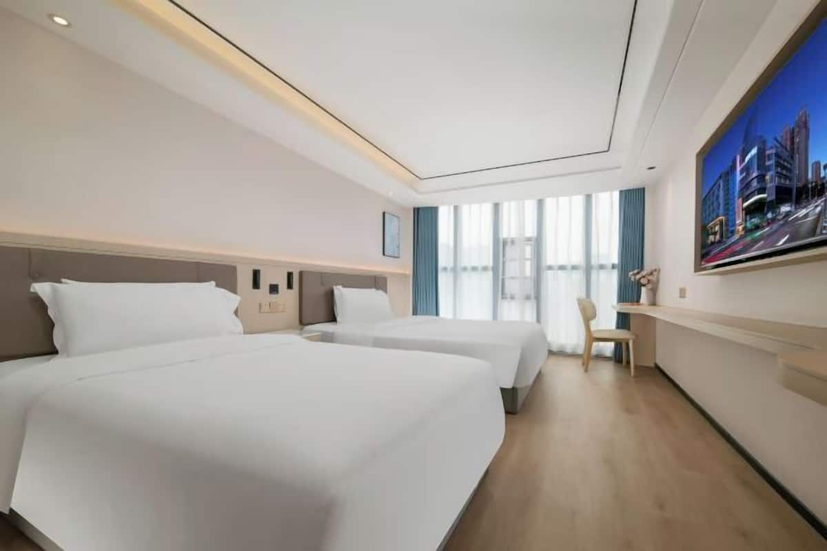 Ein Hotelzimmer mit zwei Betten, einem Schreibtisch, einem Stuhl und einem großen Fenster mit Vorhängen.
