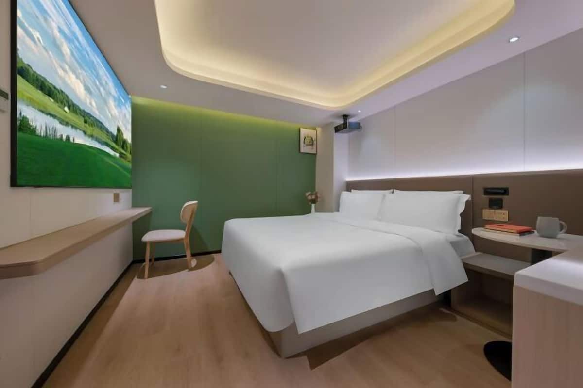 Ein modernes Hotelzimmer mit einem großen Bett, einem Schreibtisch, einem Sessel und einem Bild an der Wand.
