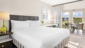 Ett hotellrum med en stor säng, ett skrivbord med en bärbar dator, en balkong med utemöbler och utsikt över omgivningen.