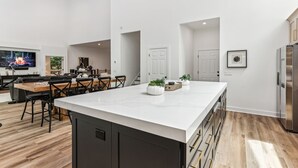 Een moderne keuken met een groot eiland, houten vloeren en een flatscreen televisie.