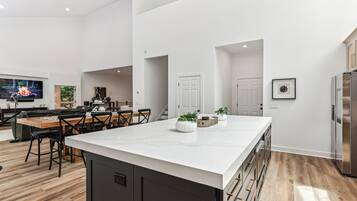 A modern kitchen with a large island, wooden flooring, and a flat-screen TV.