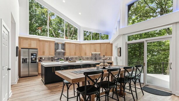 Een moderne keuken met een groot eiland, houten kastjes en uitzicht op bomen door grote ramen.