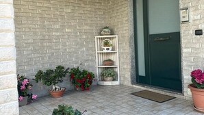 A corner of a building with a brick wall, a white shelf with potted plants, and a green door. - Garden House B&B - Vesuvius - Cozy accommodation for couples and families (Striano)