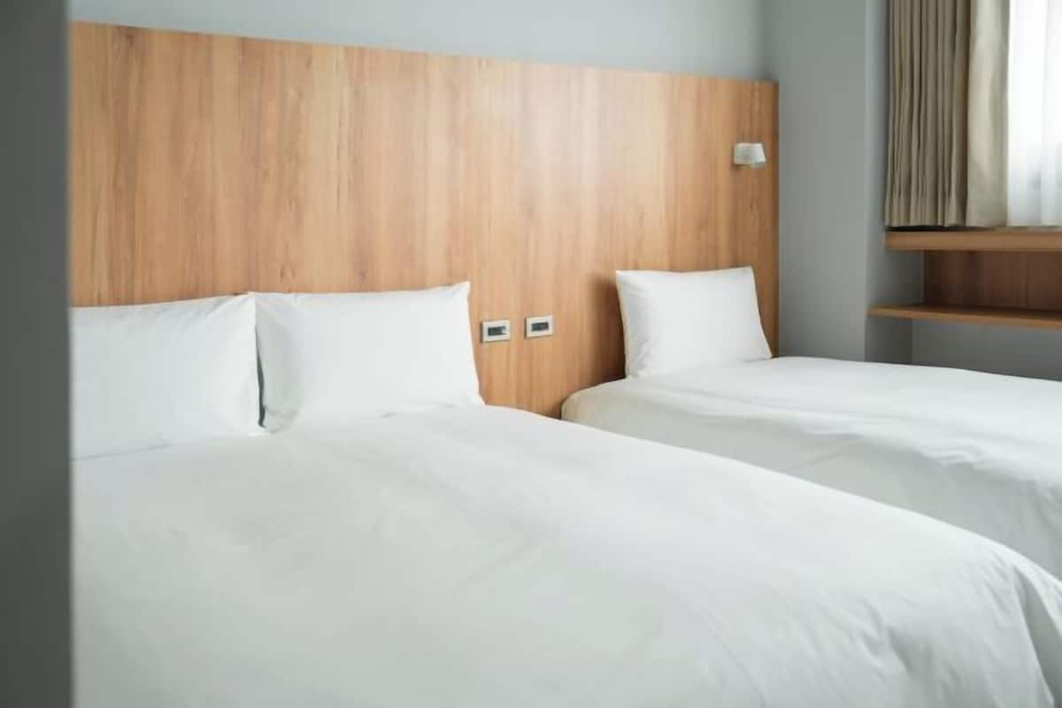 A hotel room with two beds, wooden headboard, white bedding, and a small shelf.
