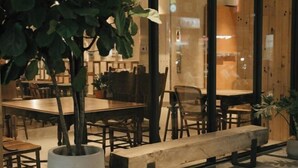 Uma área de refeições moderna com mesas e cadeiras de madeira, um banco e plantas em vasos.