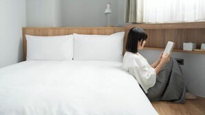 Uma pessoa sentada na cama de um quarto de hotel, lendo um livro.