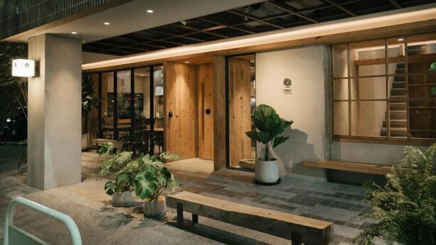 Fachada moderna de um edifício com entrada de madeira, plantas em vasos e um banco.