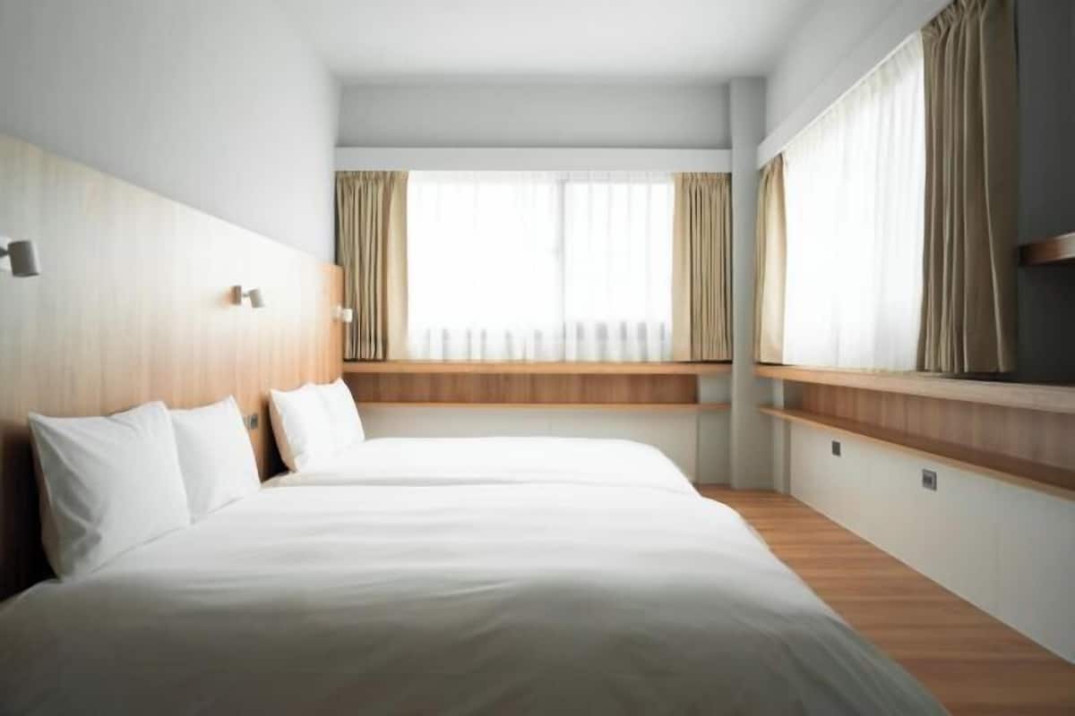 A hotel room with a large bed, a bedside table, a window with curtains, and a wooden headboard.
