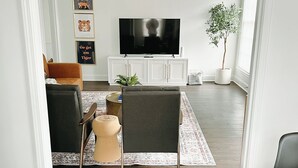 Una sala de estar con televisor, asientos y una planta en maceta.