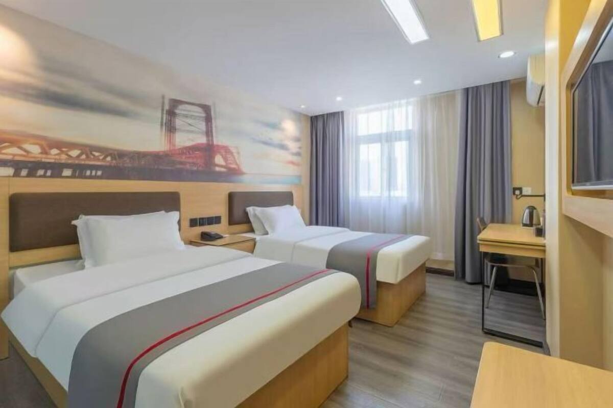 A hotel room with two beds, a desk, a chair, and a large window with curtains.