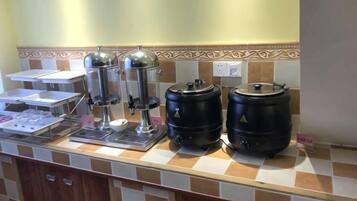 A buffet setup with coffee machines, a water dispenser, and large black containers, likely for beverages.
