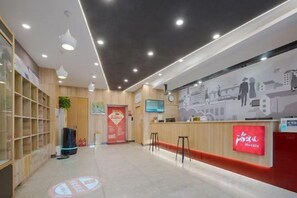 En hotellobby med en receptionsdisk, en sittgrupp och en vägg prydd med en väggmålning som föreställer en stadsbild.