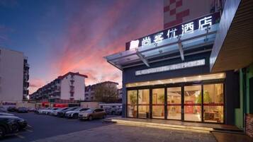 A hotel with a modern facade, large windows, and a parking lot in front.