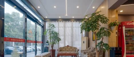 A hotel lobby with seating, a plant, a vending machine, and a view through the glass doors.
