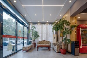 Una hall d'albergo con posti a sedere, una pianta, una macchina distributrice e vista attraverso le porte di vetro.