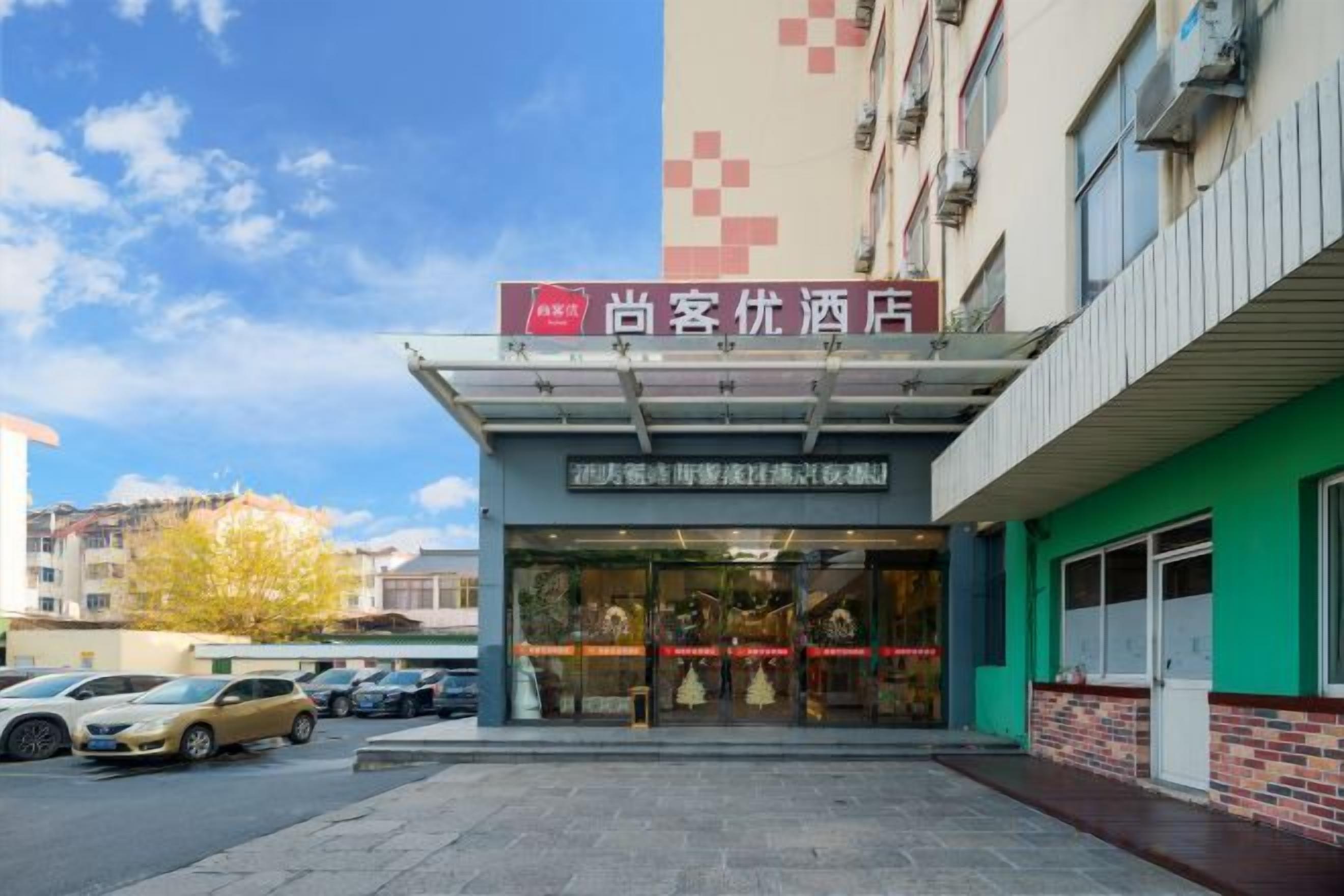 A hotel entrance with a clear sign, a covered walkway, and a parking lot with cars.